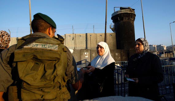 Palestinian women present their identity cards to an Israeli border police officer as they wait to make their way to Jerusalem to attend the first Friday prayer of Ramadan in al-Aqsa mosque, at Qalandia checkpoint near Ramallah