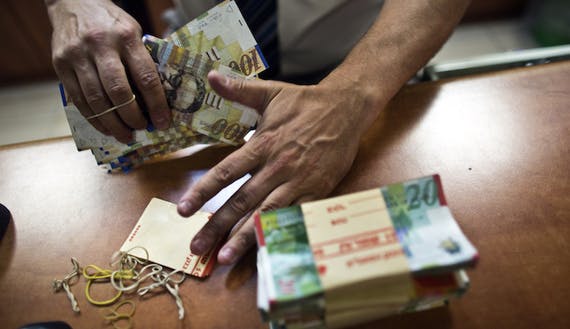 A bank employee counts Israeli Shekel notes for the camera at a bank branch in Tel Aviv