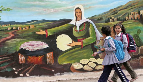 Palestinian schoolgirls walk past mural in Jenin