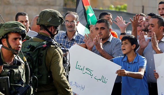 A Palestinian boy holds a sign that reads “we demand our dignity” in front of  Israeli soldiers during a protest calling for the reopening of a closed street in the West Bank city of Hebron