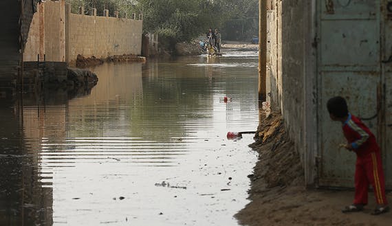 A boy looks at Palestinians as they ride a horse cart on a street flooded with sewage water from a sewage treatment facility in Gaza City