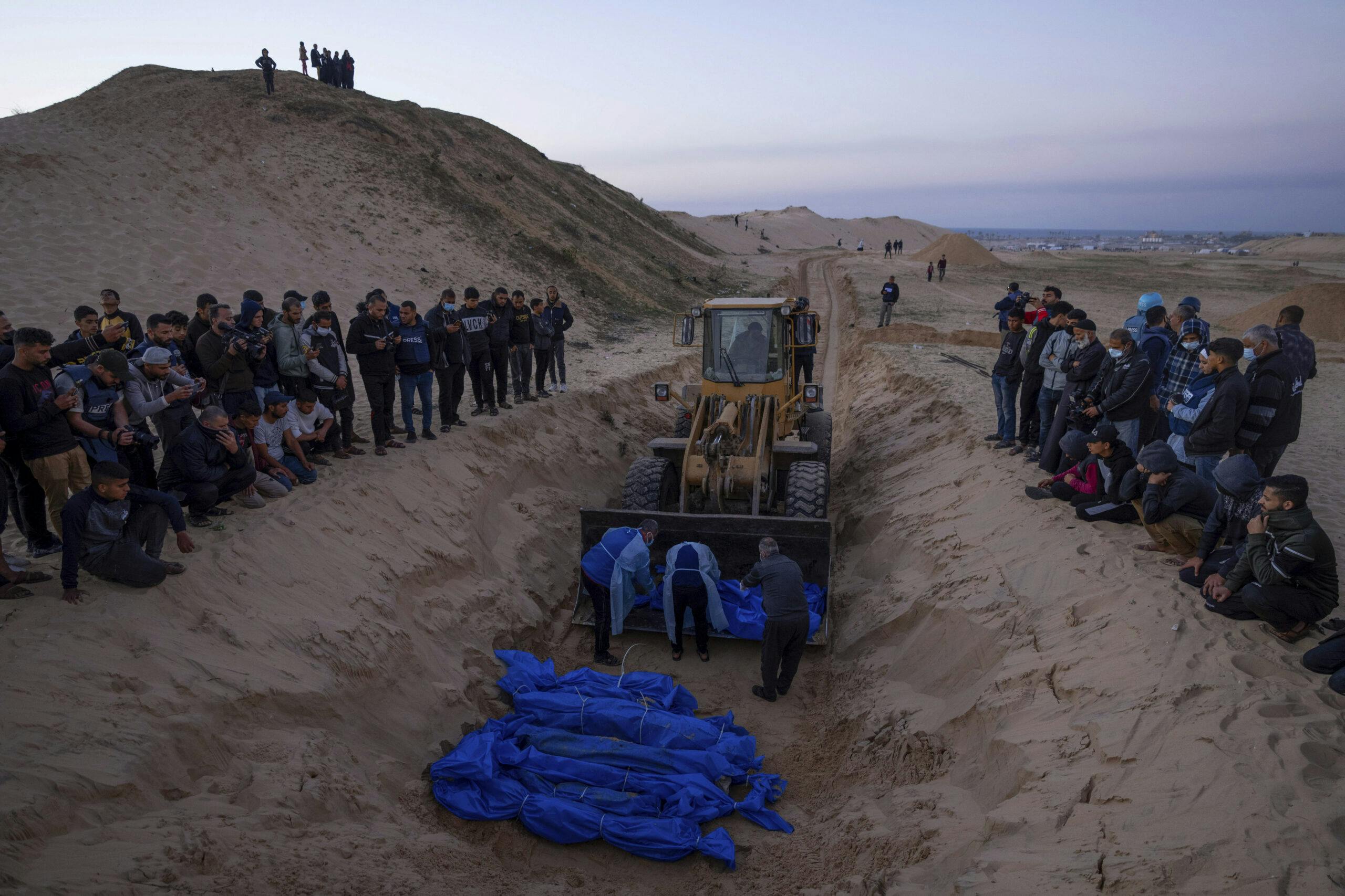 bulldozerwith bodies wrapped in blue sheets in a long grave.