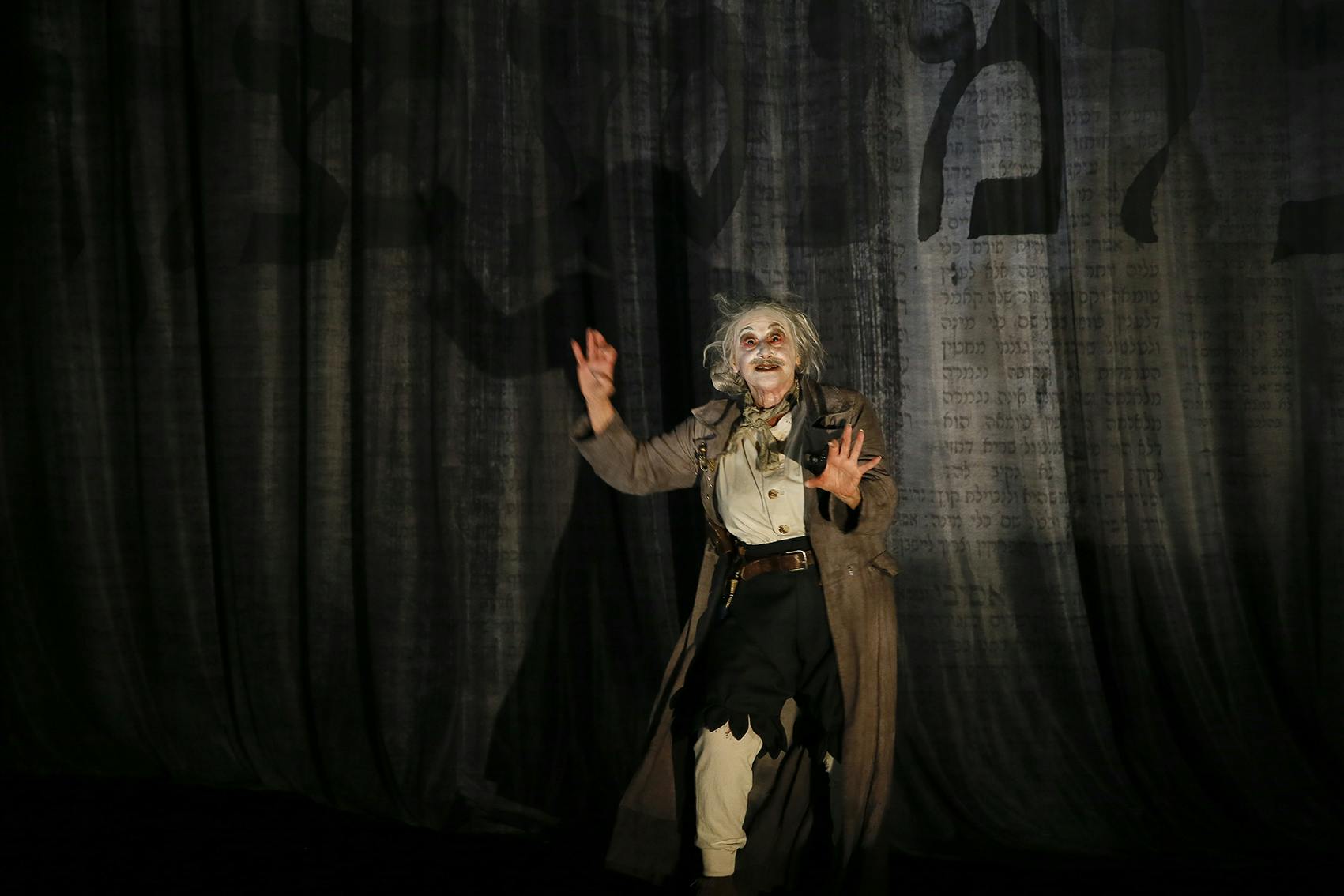 Woman in macabre costume gesturing with her hands in front of Hebrew letters