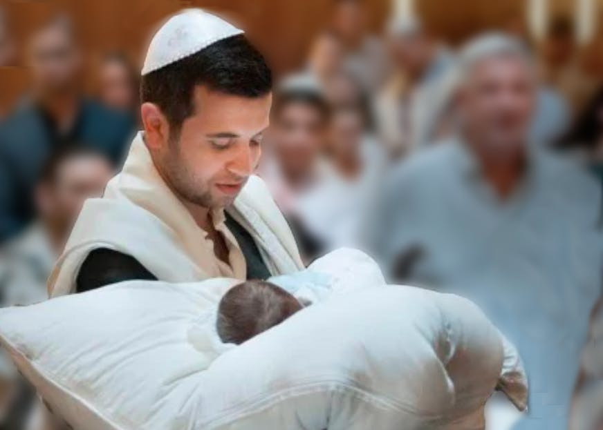 Man wearing a yarmulke and carrying a baby on a pillow