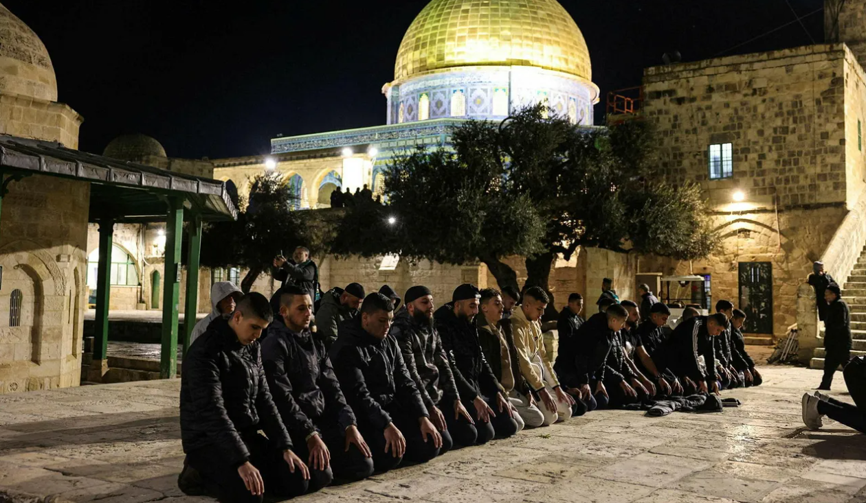 Men kneeling in front of golden dome mosque