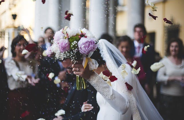 Newly married couple walking as flower petals are thrown over them.