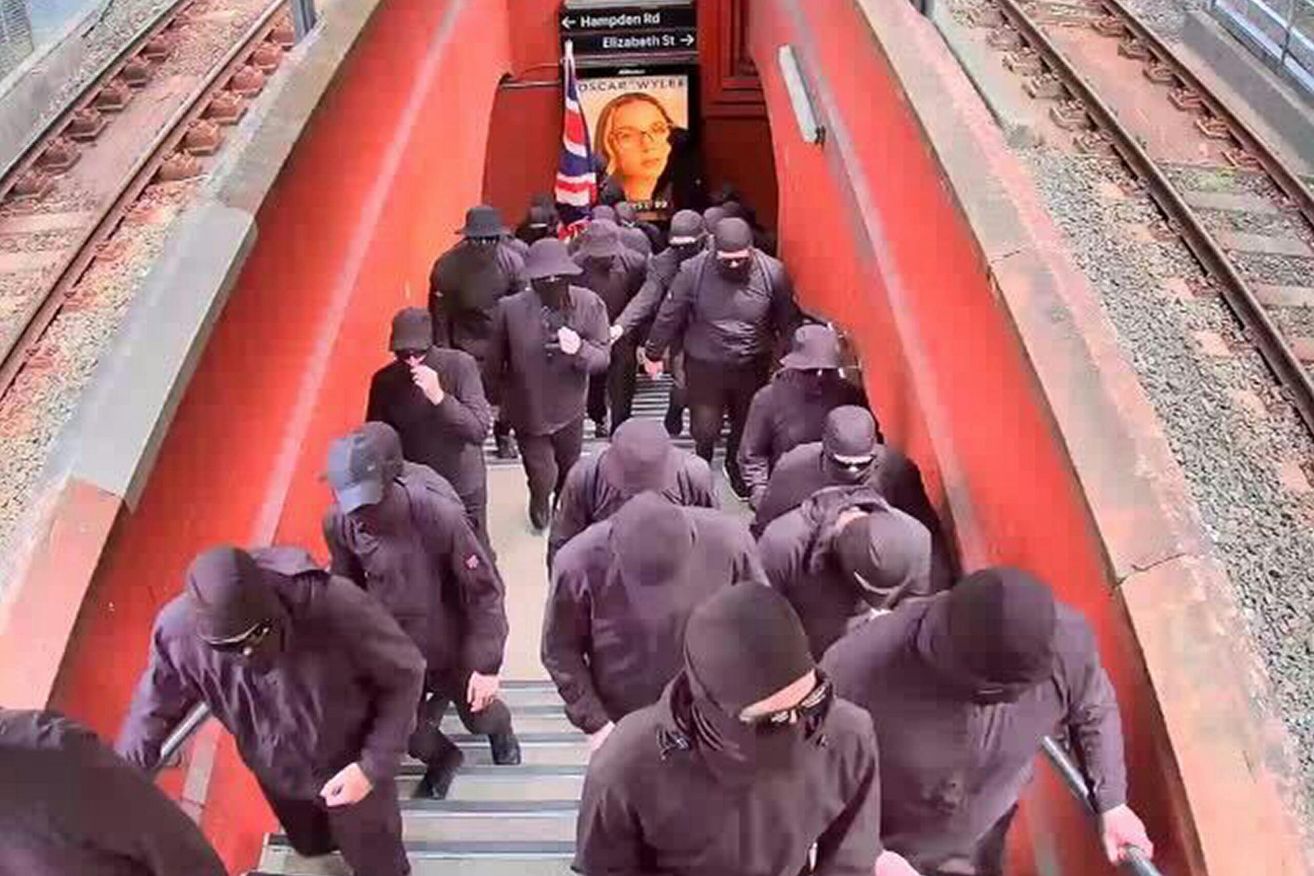 A group of about 40 men seen wearing black balaclavas and brandishing Australian flags at Artarmon train station in Sydney, Friday, January 26, 2024.