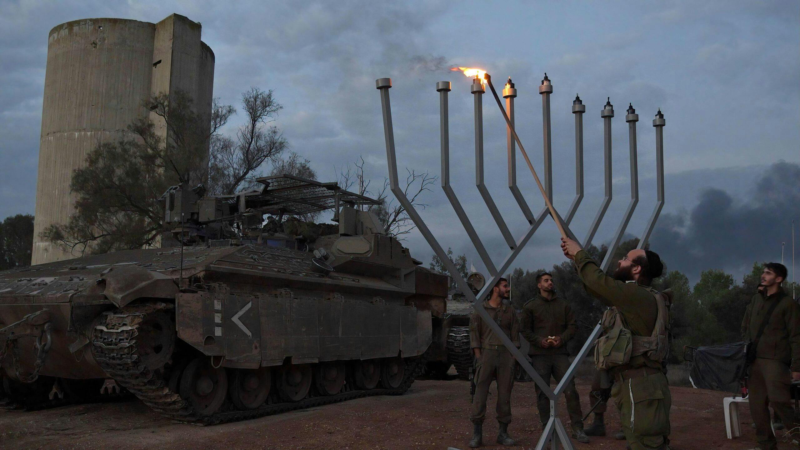 Man in army uniform lights large Chanukah menorah in front of tank
