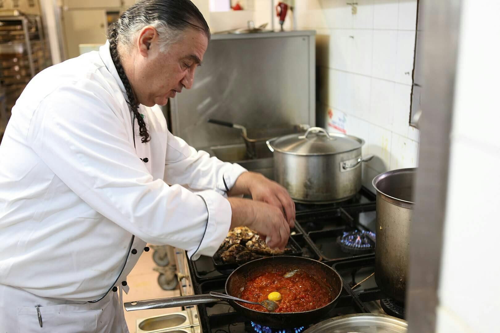 Chef cracking an egg into a pan of tomato mixture